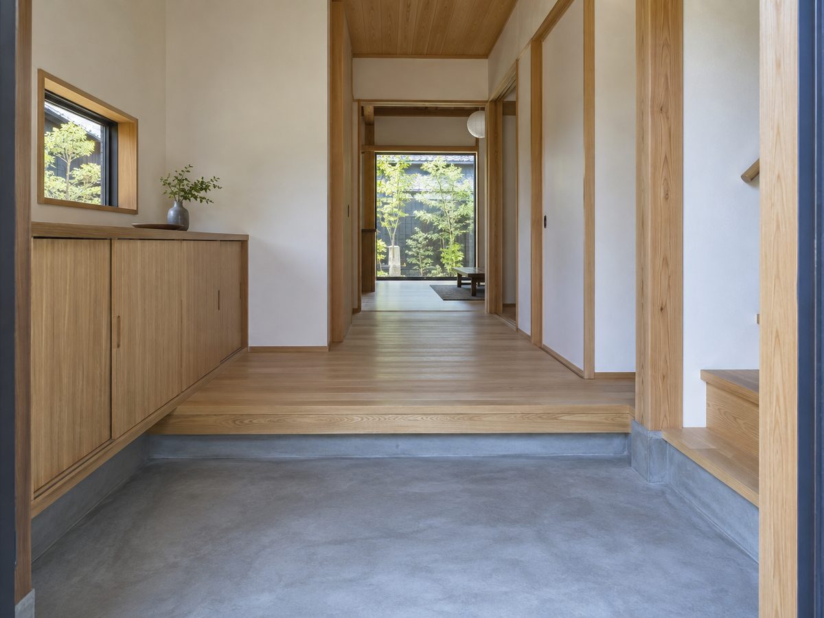 土間仕上げの玄関。コンクリートの床に造作のシューズラックが収まり、奥へ廊下が続いている。